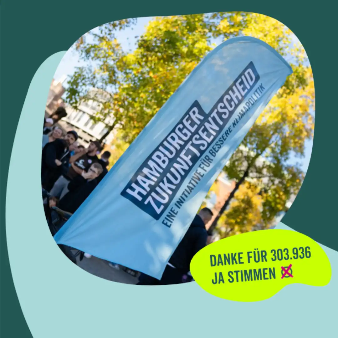 Das Bild zeigt eine Gruppe Menschen, die im Hintergrund und teilweise verdeckt durch ein Banner, auf einem begrünten Platz stehen. Auf dem Banner steht: "Hamburger Zukunftsentscheid. Eine Initiative für bessere Klimapolitik". In einer Sprechblas steht der Text: "Danke für 303.936 Ja-Stimmen".